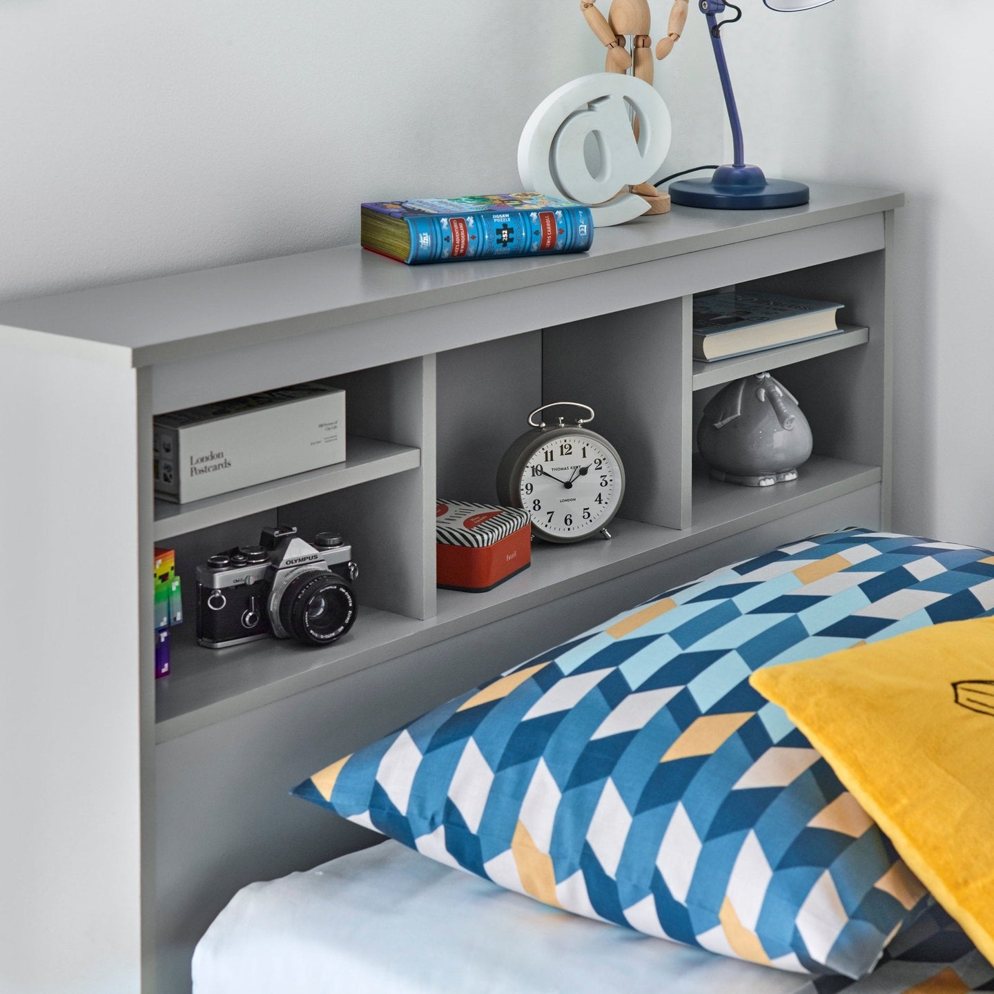 Modern gray Veera Guest Bed with headboard shelves, displaying books, clock, and decor items.